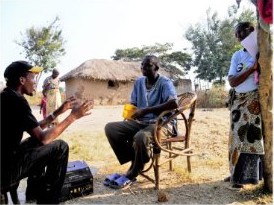 A GCS agent talks with villagers outside a thatched house