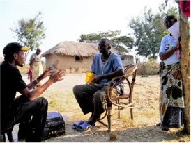 A GCS agent talks with villagers outside a thatched house